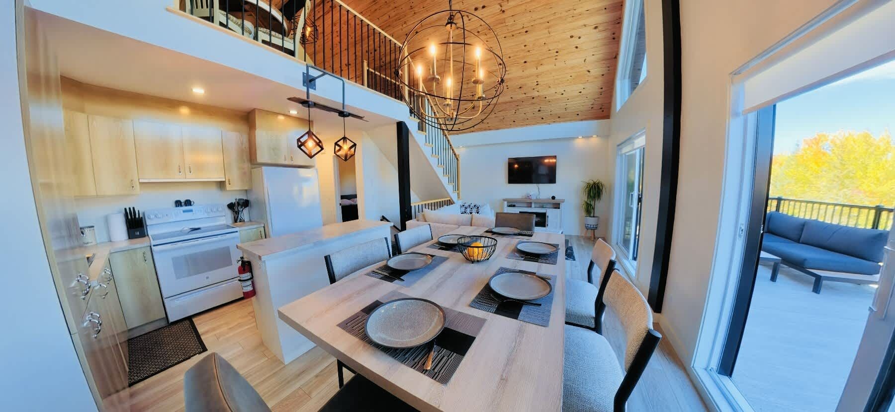 A modern kitchen with a dining area, wooden ceiling, and large windows.