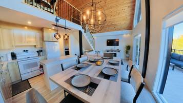 A modern kitchen with a dining area, wooden ceiling, and large windows.