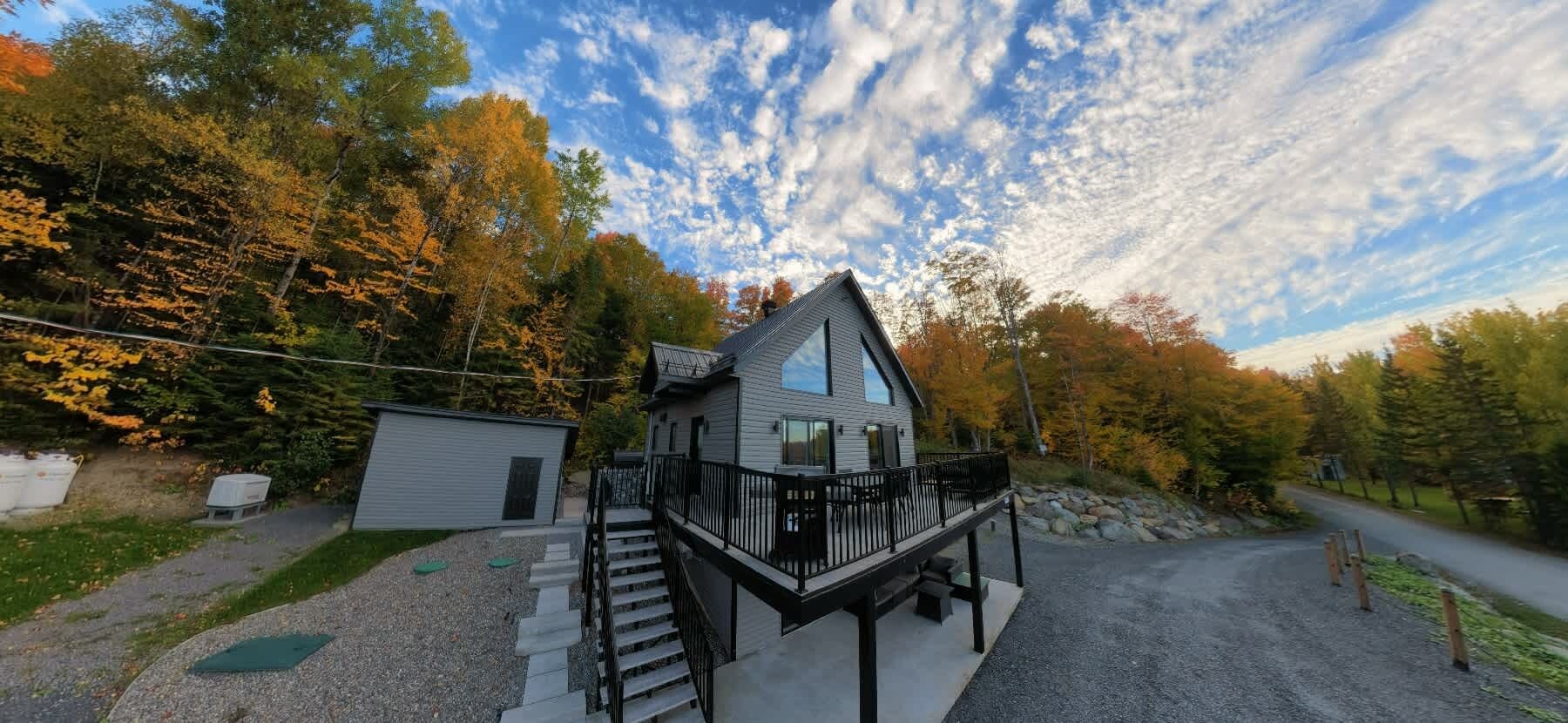 Una casa a due piani con un balcone, immersa tra alberi e con vialetto in ghiaia.