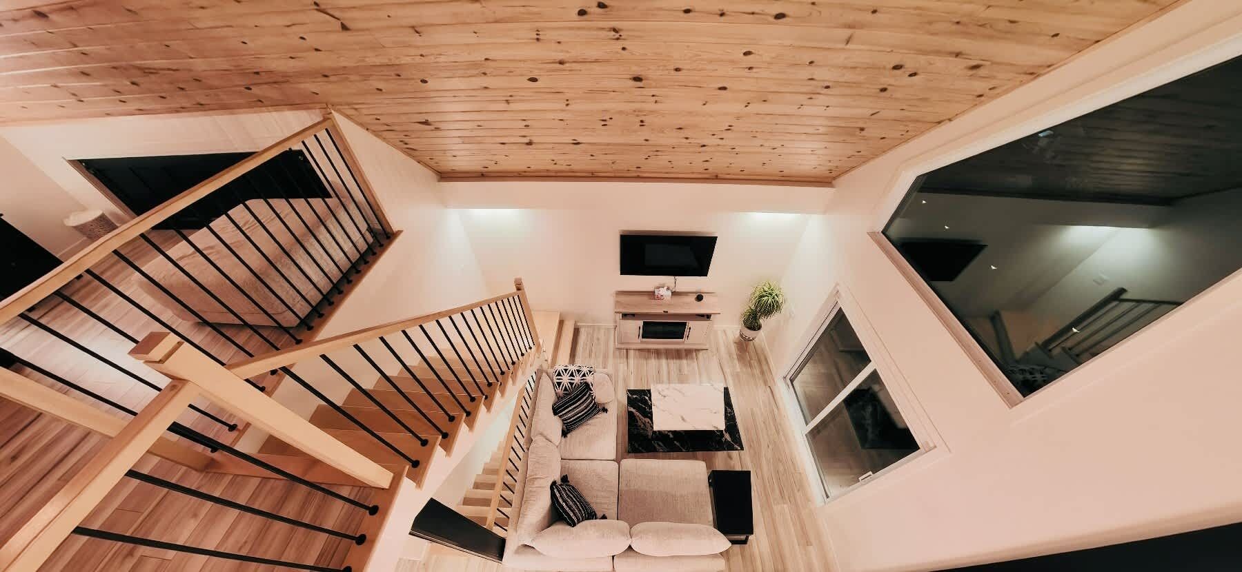 A multi-level interior with a wooden staircase, a sofa set, and a flat-screen TV.
