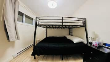 A bunk bed with a desk and lamp, a window with curtains, and a thermostat on the floor.