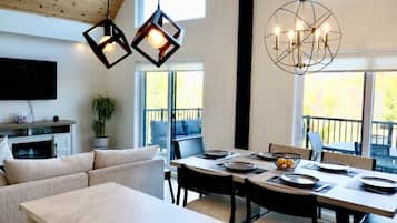 A modern dining area with a large table set for four, a television mounted on the wall, and a potted plant.