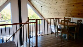 A wooden interior with a dining area, a staircase, and large windows.