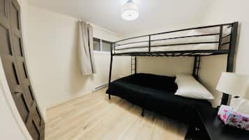 Een enkel bed met een zwart frame en witte beddengoed, een nachtkastje met een lamp, en een raam met gordijnen.