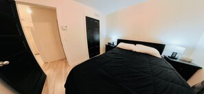 A bedroom with a black bed, a nightstand with a lamp, and a door leading to another room. - Spa, Sauna, Lake and Pool table | The Dorchester (Saint-Prosper)