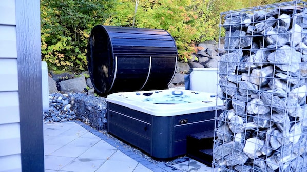 A hot tub with a stone wall and a large cylindrical object, possibly a water heater, in an outdoor setting. - Spa, Sauna, Lake and Pool table | The Dorchester (Saint-Prosper)