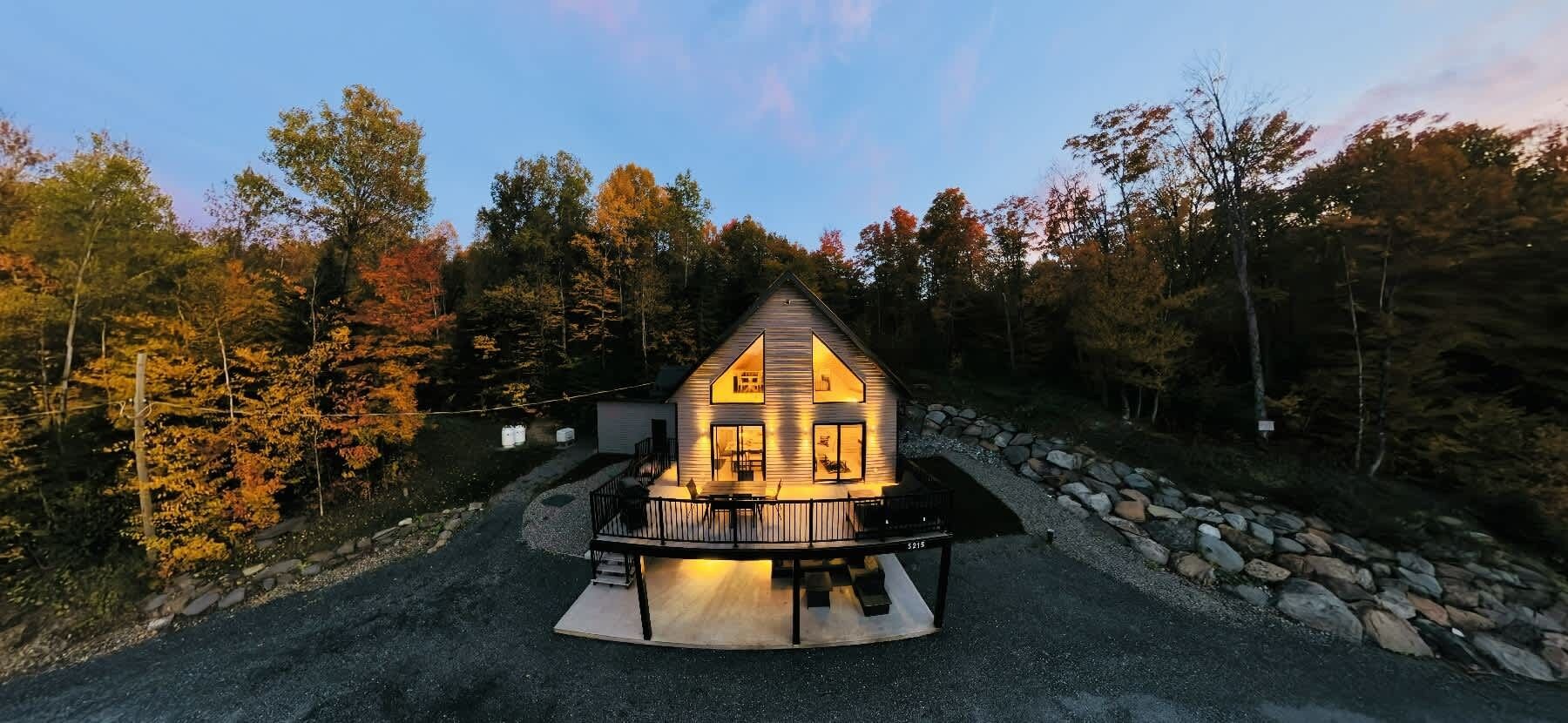 A cabin with a porch, surrounded by trees and a stone wall.