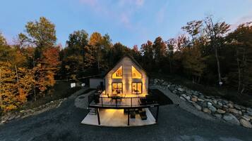 A cabin with a porch, surrounded by trees and a stone wall.