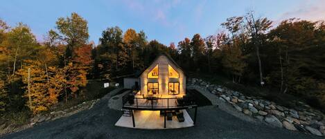 A cabin with a porch, surrounded by trees and a stone wall.
