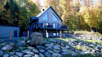 Een chalet met twee verdiepingen en een balkon, omringd door een rotsachtig landschap en herfstbomen.