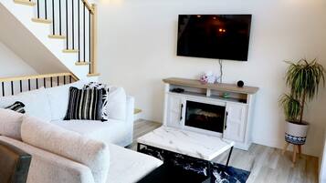 A living room with a sofa, a coffee table, a fireplace, a TV mounted on the wall, and a staircase.