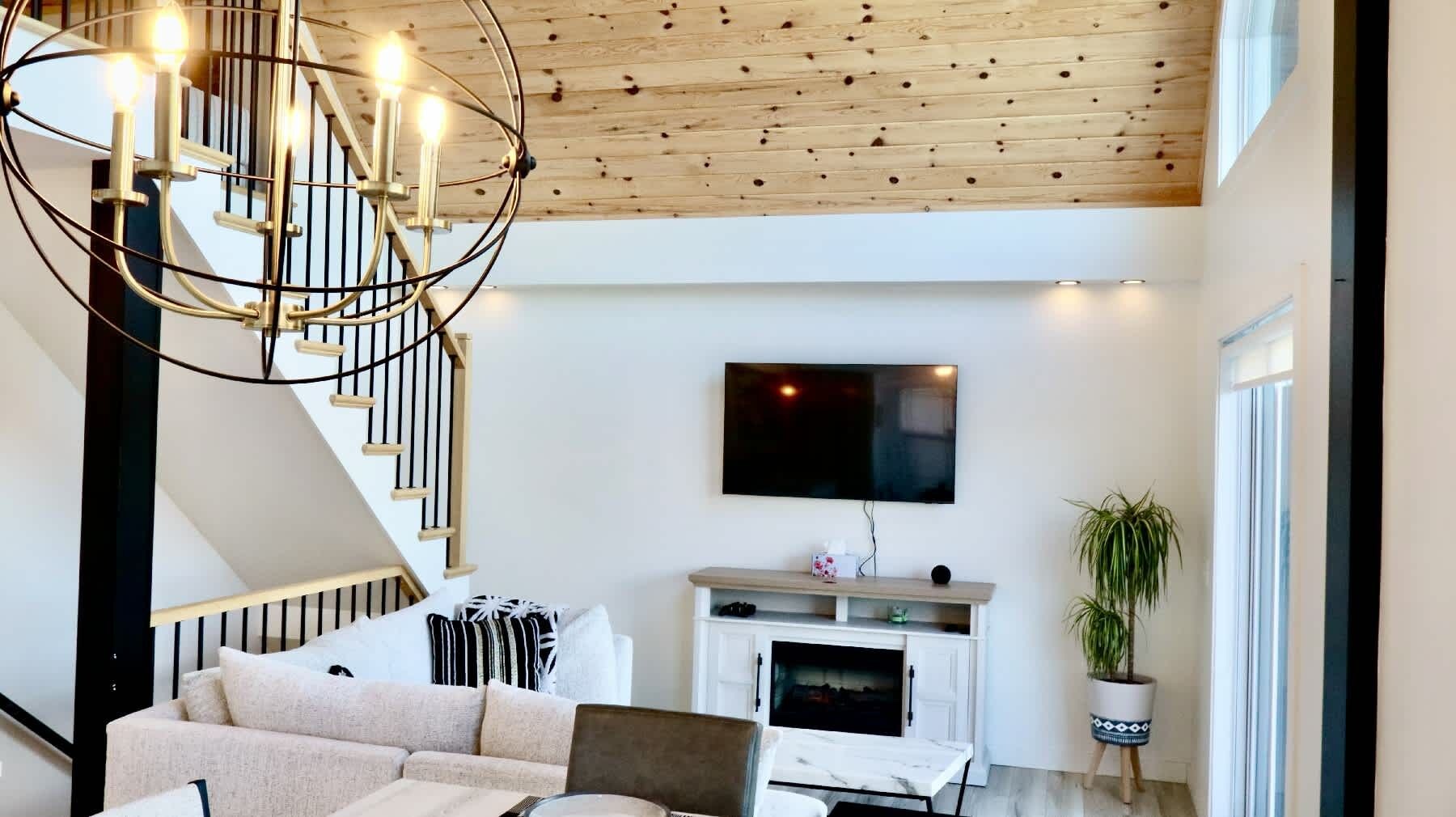 Een moderne woonkamer met een trap, een flatscreen televisie aan de muur en een kamerplant.