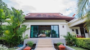 A modern house with a red-tiled roof, large glass windows, and a well-maintained garden with palm trees and shrubs. - Lotus Pool Villa Your Own Slice Of Island Paradise (Phuket)