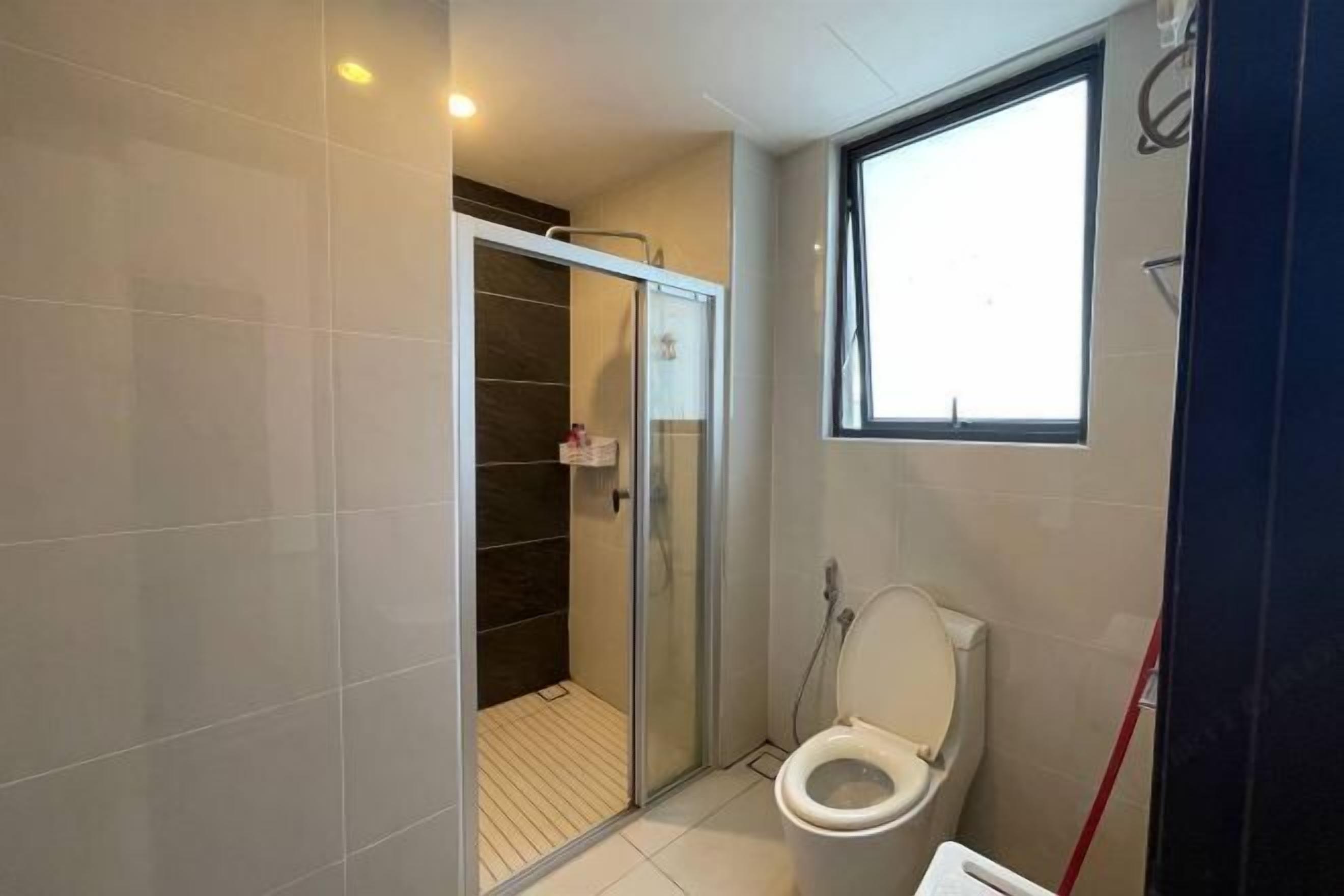 A bathroom with a glass shower enclosure, a toilet, and a window.
