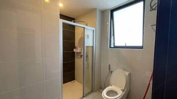 A bathroom with a glass shower enclosure, a toilet, and a window.