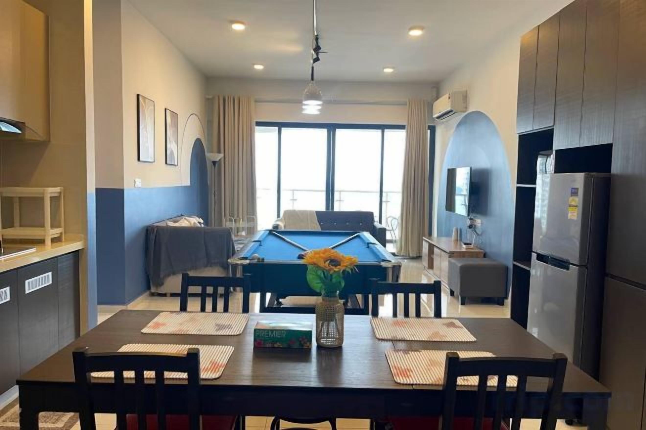 A modern living room with a pool table, dining table, and kitchen area.