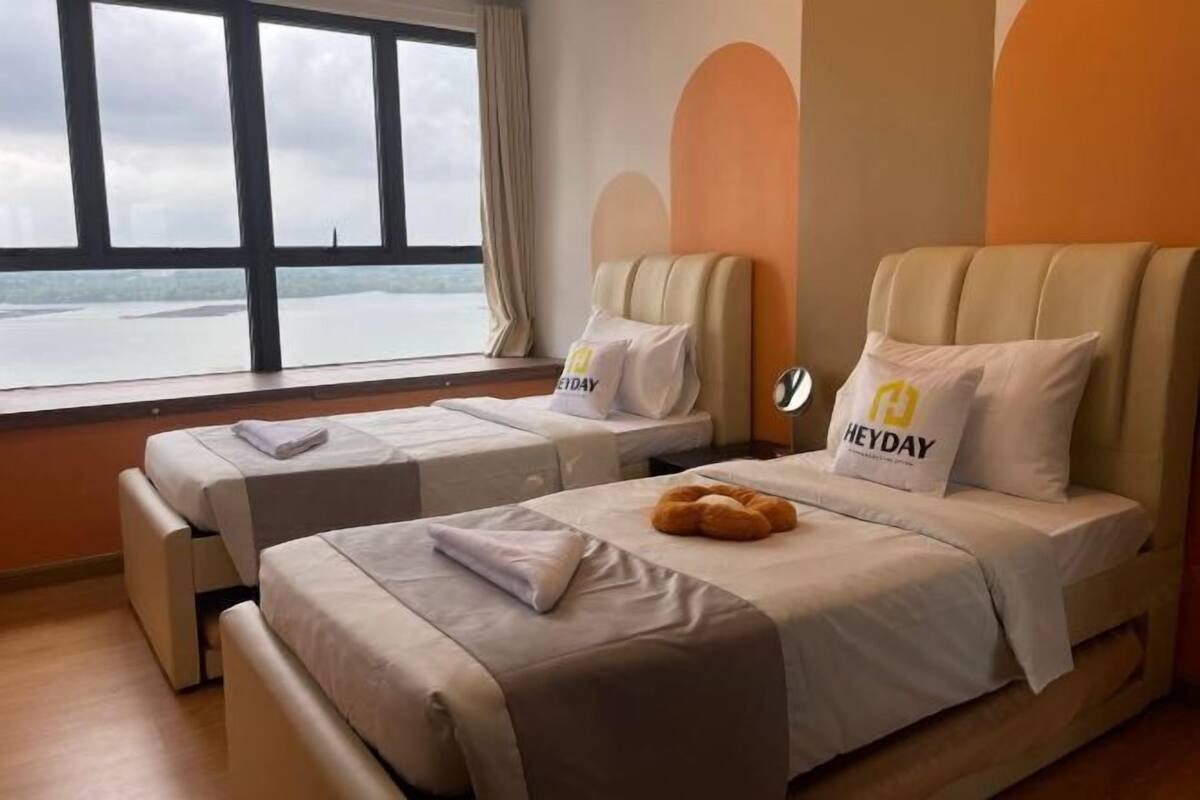 Et hotelværelse med to senge og havudsigt, med en 'HEYDAY' pude på den ene seng.