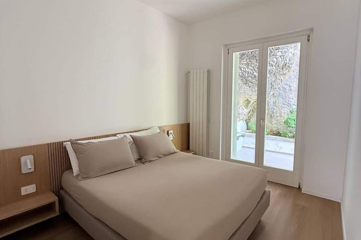 Une chambre à coucher comprenant un lit, une table de chevet, un radiateur et une porte-fenêtre coulissante donnant sur un balcon.