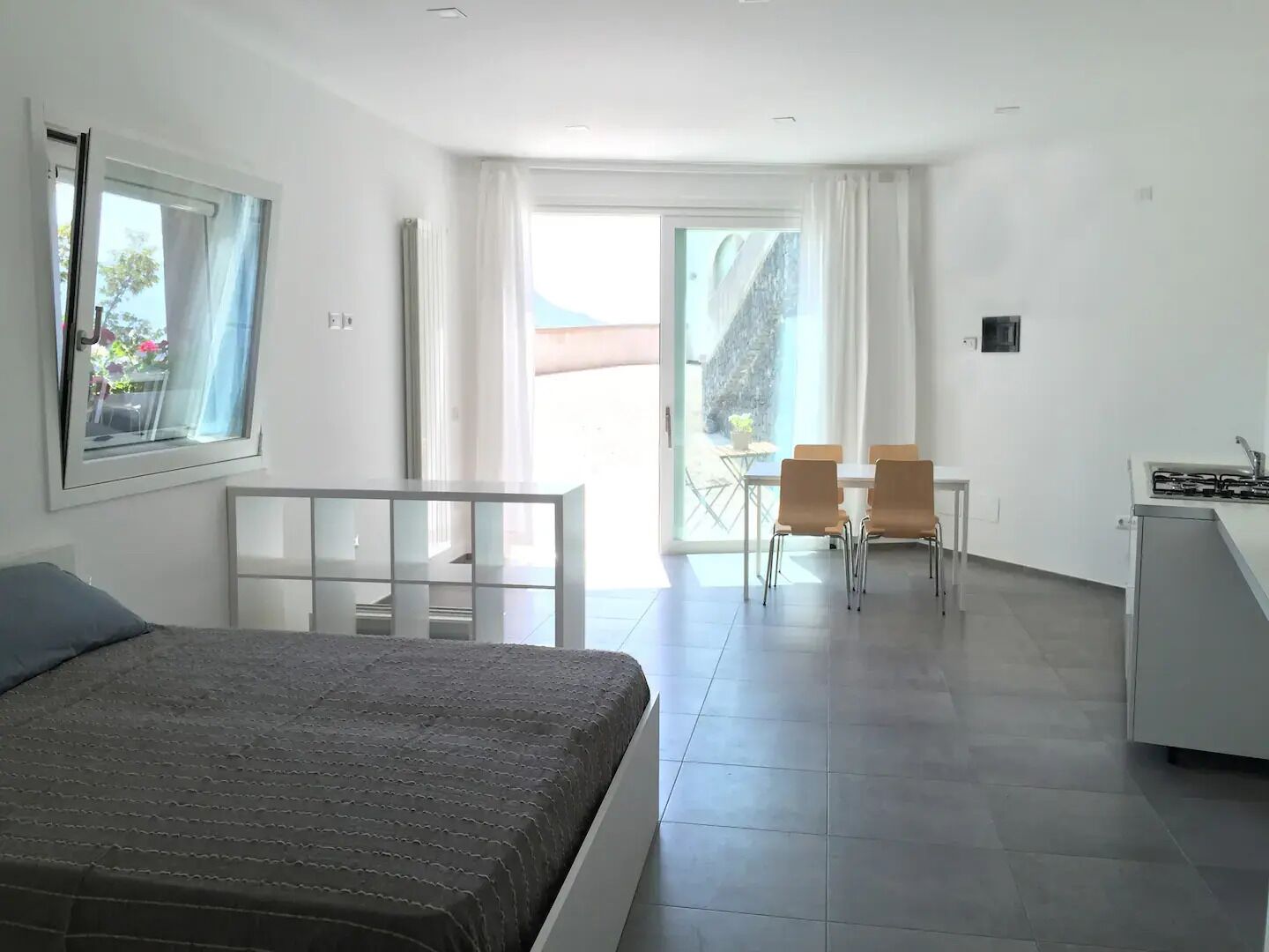 Ein Hotelzimmer mit Bett, Schreibtisch mit Stuhl, einer kleinen Küchenzeile und einem Balkon mit Tisch und Stühlen.