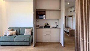 A modern apartment with a kitchenette, a green sofa, and a wooden floor.