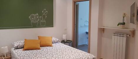 Una camera da letto con un letto, un comodino, un tavolo di appoggio, un termosifone, una finestra e una porta che dà su un balcone.