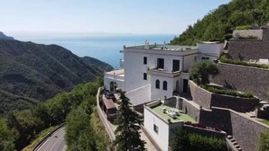 A white building with a flat roof, located on a hillside with a view of the sea.