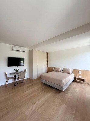 A modern bedroom with a bed, a TV, a desk with chairs, and built-in wardrobes.