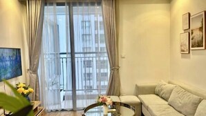 A living room with a sofa, a glass coffee table, a TV, and a large window with curtains. - Vinhomes Time city & Park Hill - Green Home (Hanoi)
