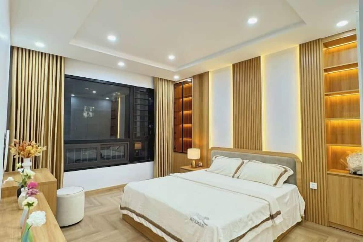 A modern hotel room with a large bed, bedside tables, a desk, and a window with curtains.