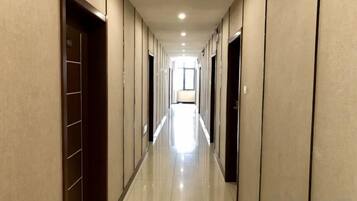 A hotel corridor with doors on both sides, a tiled floor, and a light source at the end.