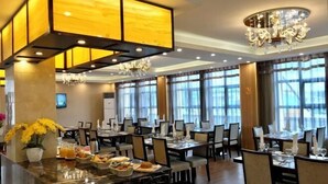 A spacious dining area with multiple tables and chairs, a marble bar with food and drinks, and large windows allowing natural light. - Hotel l'Orchidee Owendo (Libreville)