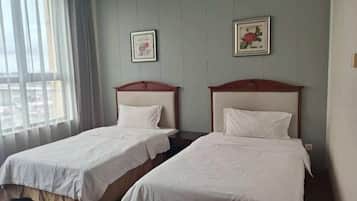 Ein Hotelzimmer mit zwei Einzelbetten, einem großen Fenster mit transparenten Vorhängen und zwei gerahmten Bildern an der Wand.
