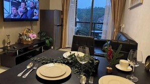Un coin repas avec une table dressée pour deux personnes, un téléviseur fixé au mur et une vue sur l’extérieur grâce à une grande fenêtre.