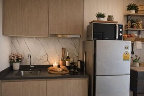 Une cuisine avec des meubles en bois, un dosseret en marbre, un réfrigérateur en acier inoxydable et une petite plante en pot posée sur le comptoir.