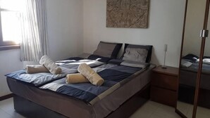 A bedroom with a bed, pillows, a bedside table, a mirror, and a window with curtains.