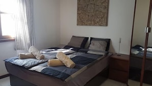 A bedroom with a bed, a bedside table, a mirror, and a wall art piece.