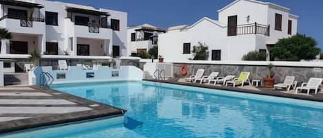 Una piscina con sillones de descanso y un edificio con balcones.