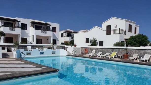 A swimming pool with lounge chairs, white buildings, and a clear sky.
