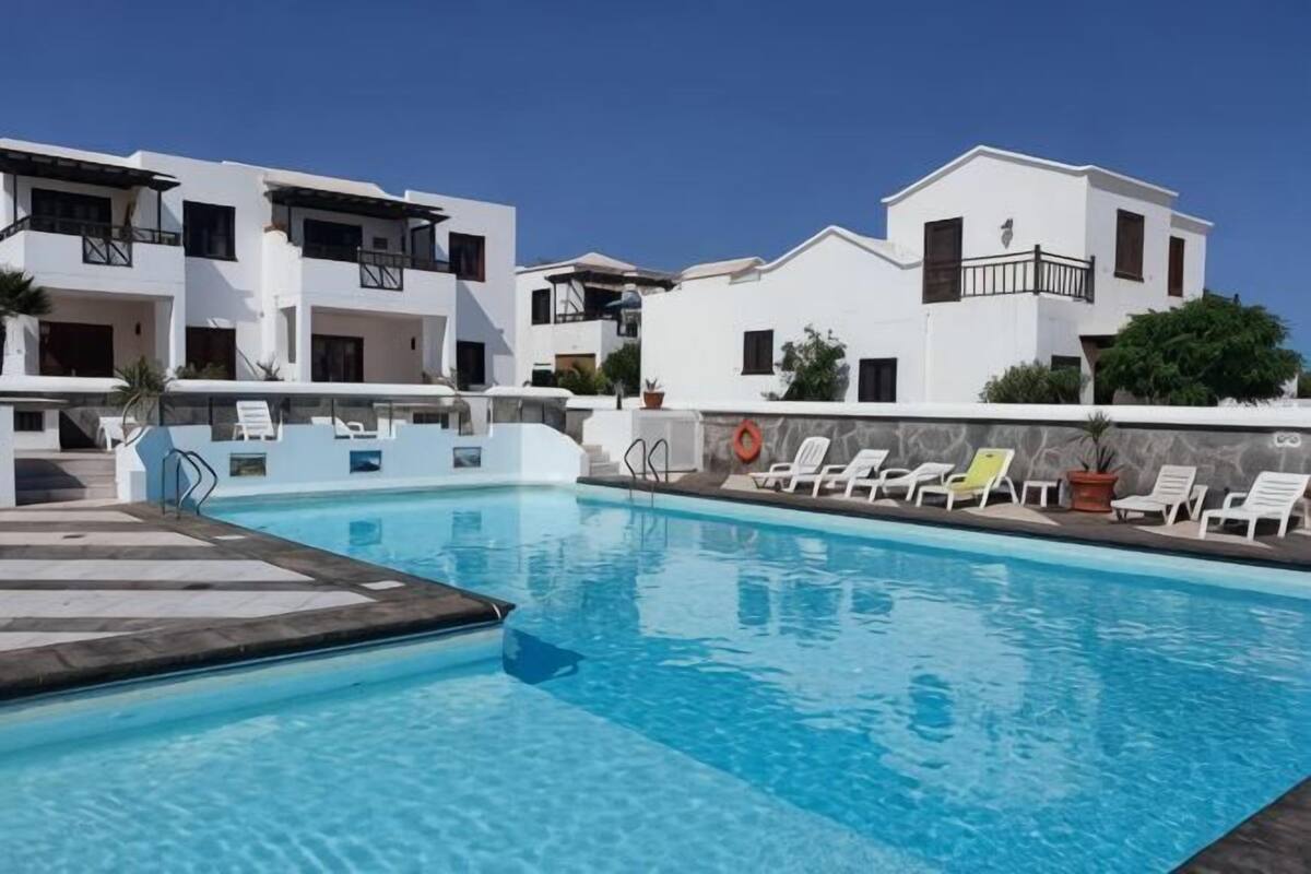 A swimming pool with lounge chairs, white buildings, and a clear sky.