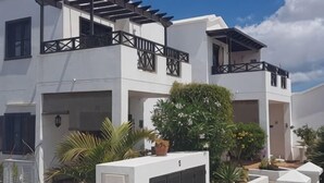 A modern two-story building with balconies, white walls, and potted plants.
