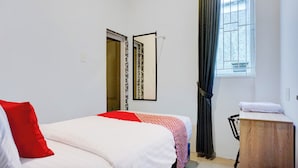 Une chambre à coucher comprenant un lit, une table de chevet en bois, un miroir, une fenêtre avec des rideaux et une porte ornée d’un motif.