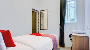 Une chambre à coucher comprenant un lit, une table de chevet en bois, un miroir, une fenêtre avec des rideaux et une porte ornée d’un motif.
