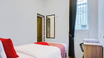 Ein Schlafzimmer mit einem Bett, einem Nachttisch aus Holz, einem Spiegel, einem Fenster mit Vorhängen und einer Tür mit Musterdesign.