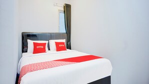 Un lit bien fait, avec une literie blanche et rouge, une tête de lit noire et deux oreillers sur lesquels est inscrit le mot « OYO ».
