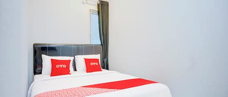A neatly made bed with white and red bedding, a black headboard, and two pillows with the word "OYO" on them.