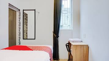 A bedroom with a bed, a desk, a mirror, and a window with curtains.