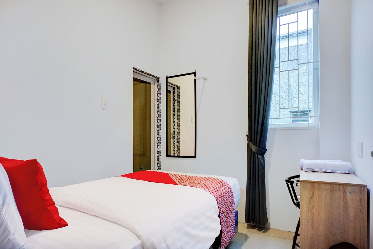 Un dormitorio con cama, una mesita de noche de madera, un espejo, una ventana con cortinas y una puerta con diseño decorativo.