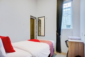 A bedroom with a bed, a wooden nightstand, a mirror, a window with curtains, and a door with a patterned design. - Collection O Almasarra Resid Near Ring Rd Medan (Medan)