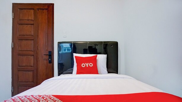 Een hotelkamer met een houten deur, een zwart hoofdeinde en een bed met een rood-witte dekbedovertrek en kussens.