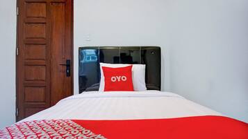 Habitación de hotel con puerta de madera, cabecero negro y cama con colcha y almohadas rojas y blancas.